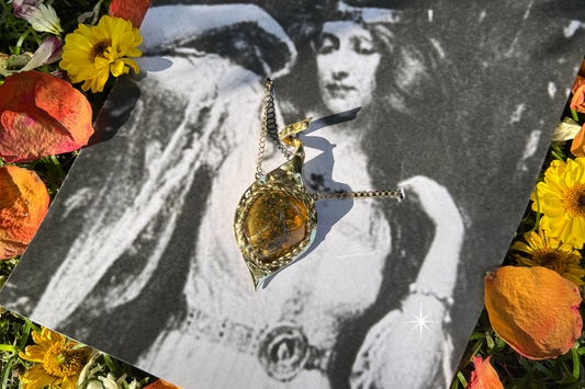 Flores verano y una imagen de la Diosa Freya con su collar Brisingamen dorado en forma de gota de amuleto y una amatista con inclusiones